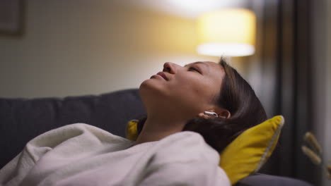 close up of woman spending evening at home on sofa wearing wireless earbuds and streaming music or podcast from mobile phone 6