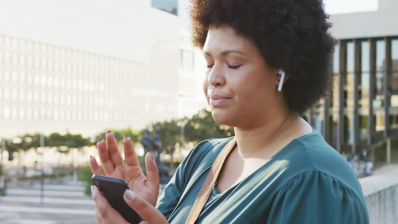 Happy plus size biracial woman using smartphone and wearing earphones in city
