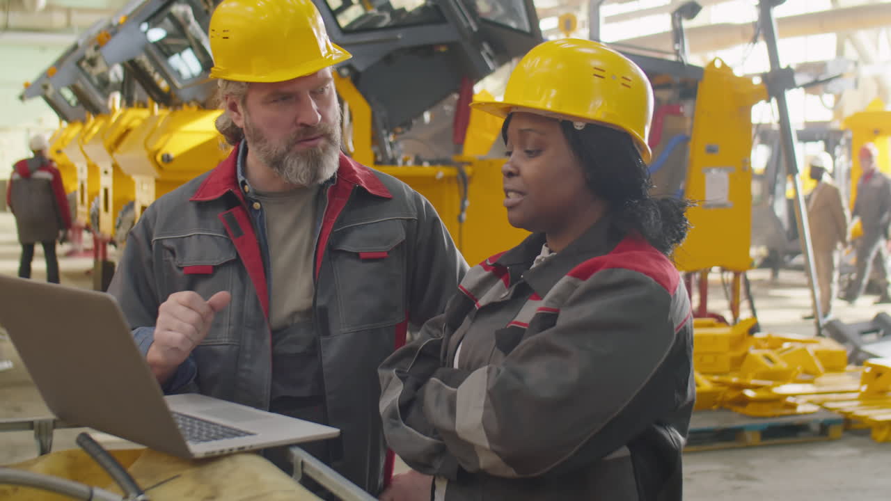 Diverse Factory Workers Using Laptop and Speaking
