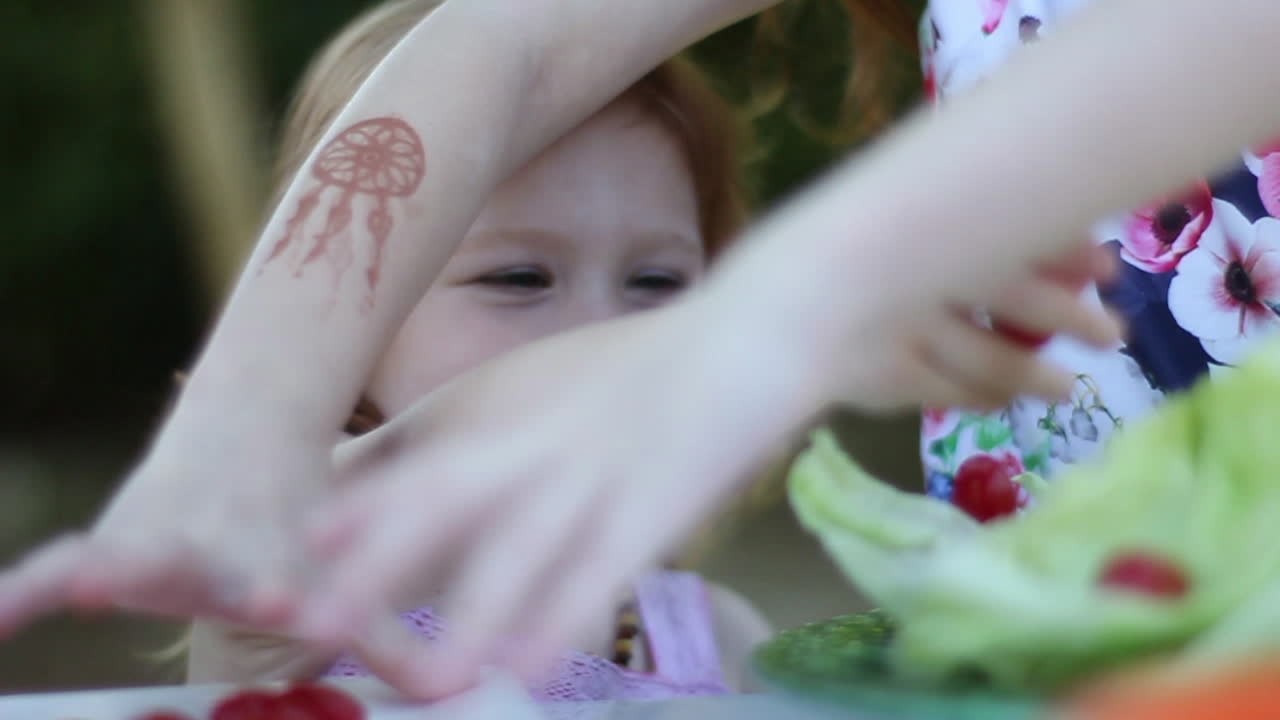 Menina pré-escolar sorrindo e adicionando alegremente tomates-cereja a uma salada em piquenique no quintal
