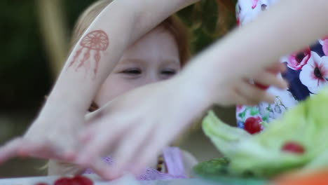 pre-schooler girl smiling and joyfully adding cherry tomatoes to a salad in the backyard picnic