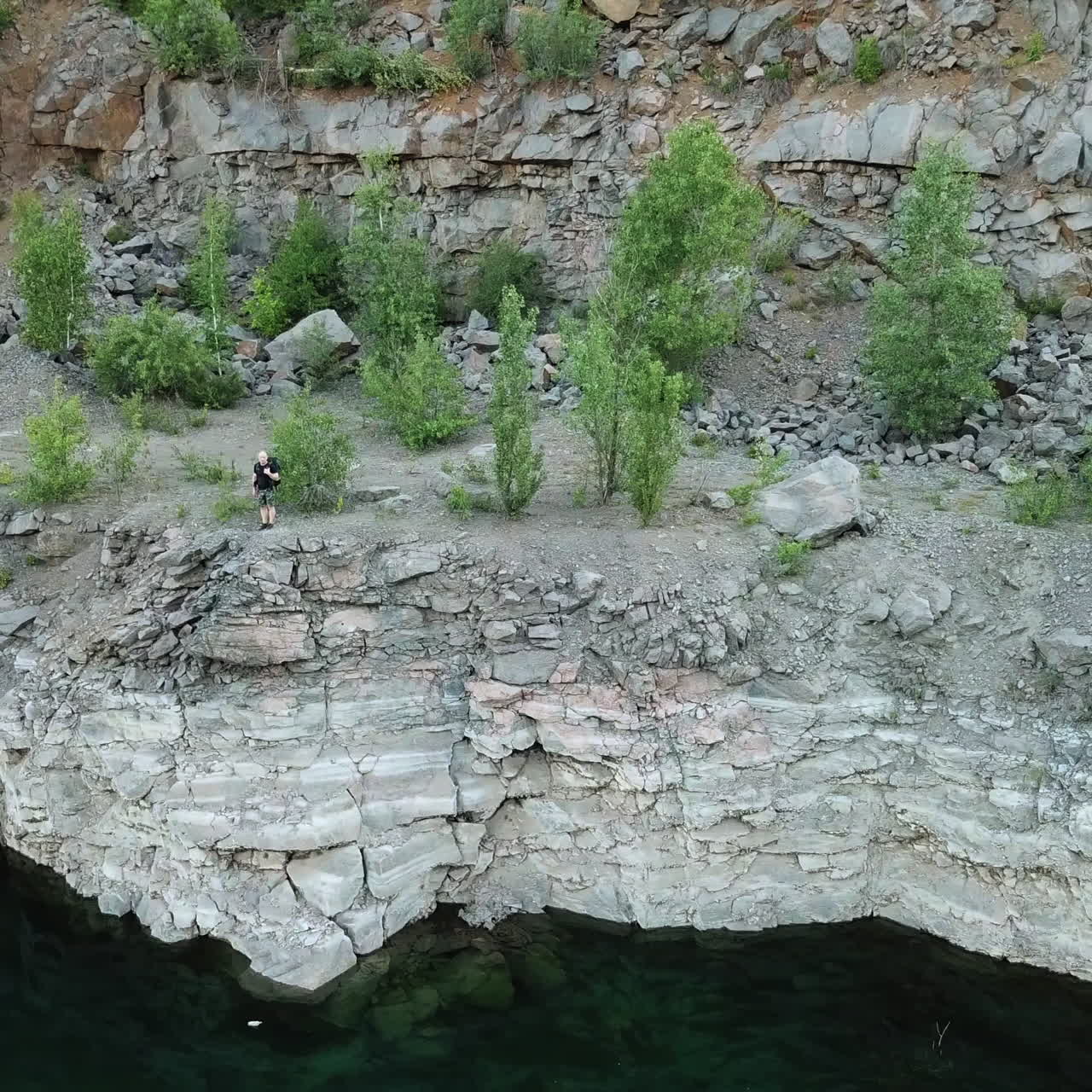 Clean water background near the stone slope and the tourist walking on it. Aerial filming of a rocky canyon with a wanderer outdoors. Motion bottom up