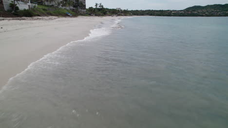drone volando bajo disparado justo por encima de la playa de careyeros, capturando la costa donde las olas se encuentran con la arena