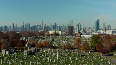 Vorwärtsflug-über-Historischem-Kalvarienberg-Friedhof.-Alte-Grabsteine-Auf-Grünem-Rasen-Zwischen-Herbstfarbenen-Bäumen.-Skyline-Mit-Manhattan-Wolkenkratzern.-Königinnen,-New-York-City,-USA