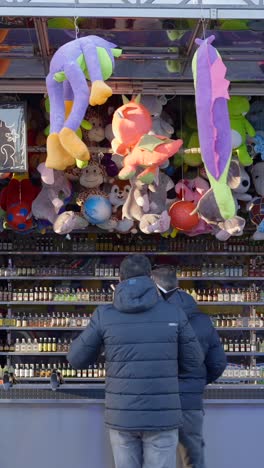 men playing a carnival game at a stall with plush toys and liquor bottle prizes