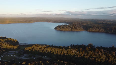 Drone-view-of-lake-Mahinapua-in-between-forests-during-sunset-at-Hokitika,-West-Coast,-New-Zealand