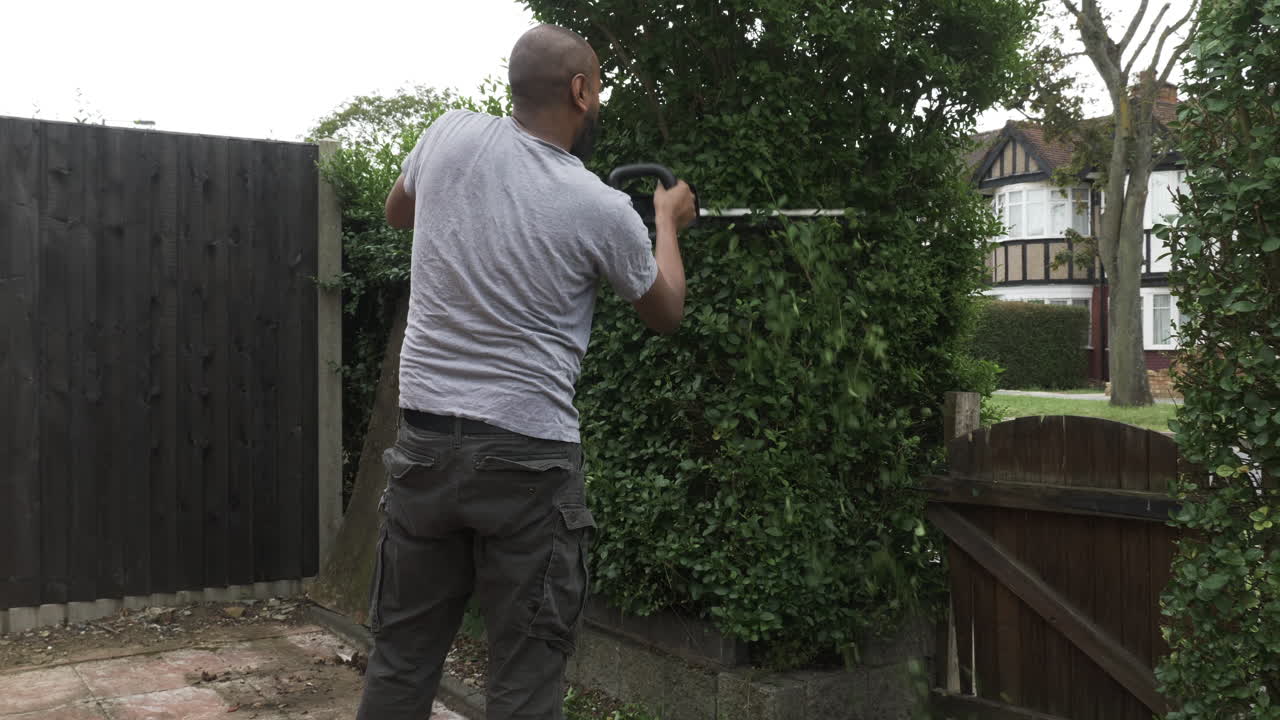 reino unido macho calvo adulto asiático usando un cortasetos eléctrico afuera en el jardín delantero