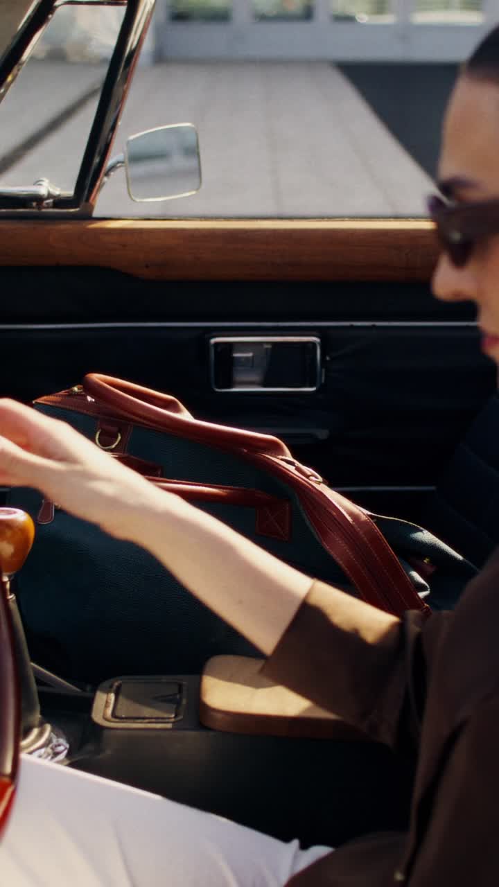 Woman driving a vintage convertible with a stylish travel bag