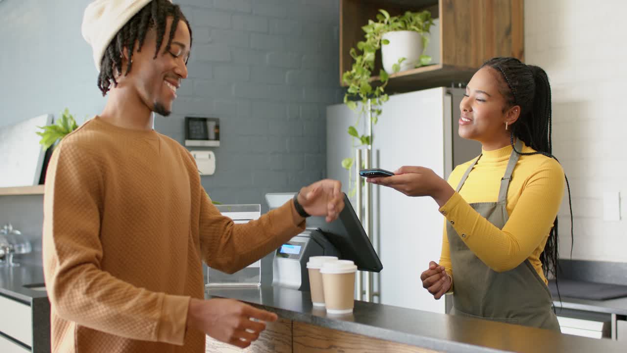 Cliente afroamericano che utilizza uno smartwatch in un bar, barista che scansiona lo smartwatch e consegna le tazze