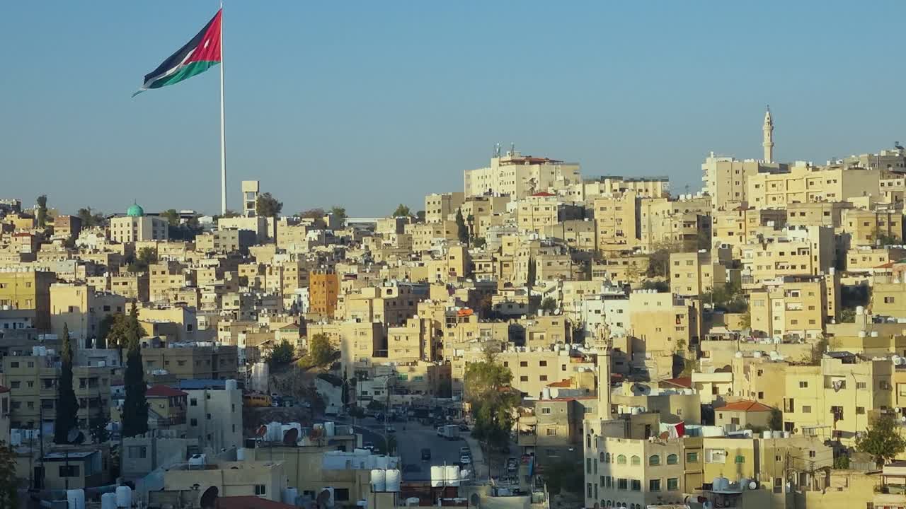 Tramonto panoramico su Amman, Giordania, con luce calda sui tetti, una bandiera in cima alla collina ben visibile, architettura tradizionale e uccelli che volano attraverso un cielo sereno al crepuscolo