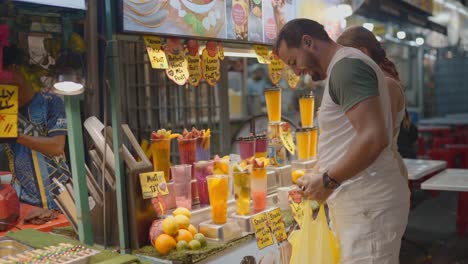 Visitors buying fresh fruit juice from roadside stall in Kuala Lumpur city in Malaysia.