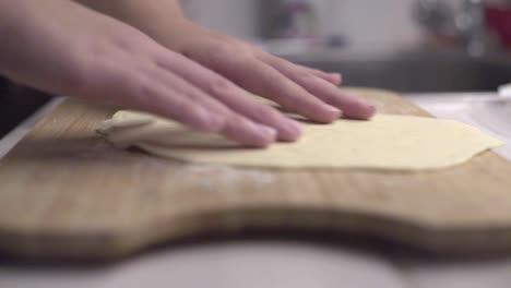 hands turning over thin disk of dough and tapping it gently onto wooden board