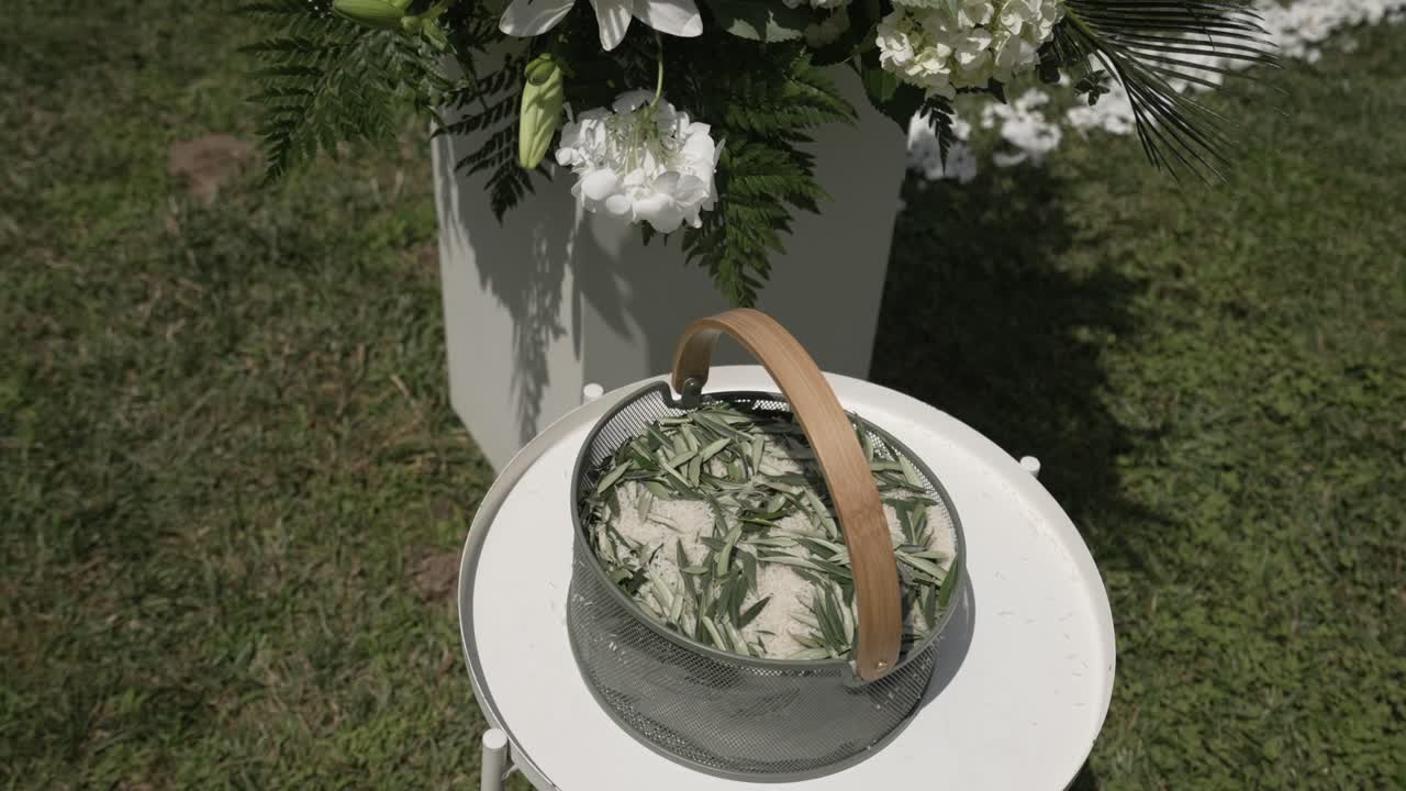 Simple basket of rosemary leaves placed on a white stand, part of an outdoor wedding decor