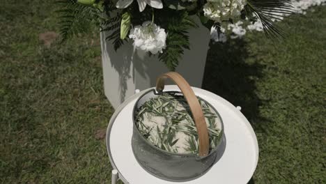 simple basket of rosemary leaves placed on a white stand, part of an outdoor wedding decor