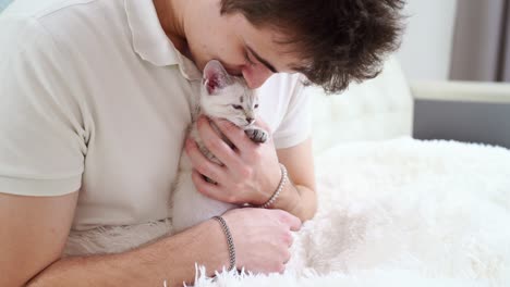 a young man holds a small white kitten and kisses him. nevsky masquerade cat.
