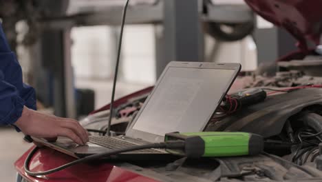 computer diagnostics of cars, young mechanic specialist male uses laptop technology while repairing vehicle with open hood at service station