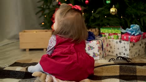 baby girl sitting by christmas tree with gifts