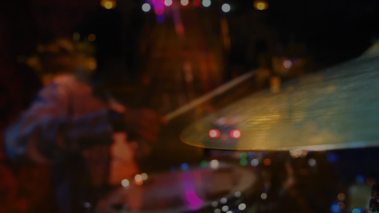 Batterista che fa roteare la bacchetta e poi colpisce un piatto ride sotto i riflettori della musica dal vivo, aumentando l'intensità
