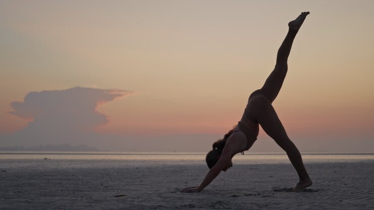 Mujer practicando posturas de yoga en una playa al atardecer