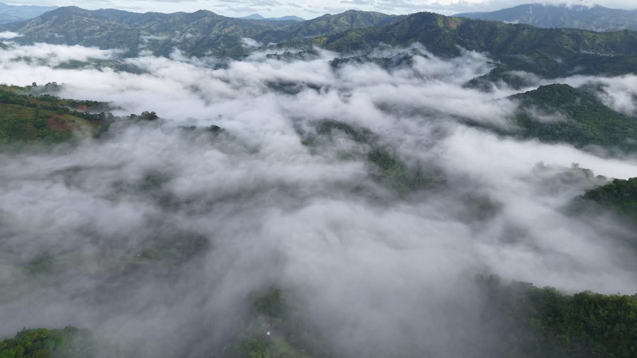 Mystic cloudscape over forest landscape of Ocoa in Dominican Republic. Mountain range in distance. Aerial wide shot. Dense white clouds over treetops