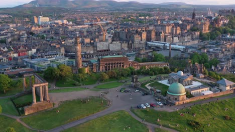 Aerial-rotating-shot-around-the-National-Monument-of-Scotland-with-people-sitting-in-the-park,-Edinburgh-drone-highlights,-nelson-monument-on-Calton-hill