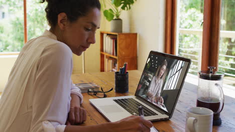 biracial businesswoman sitting at desk using laptop having video call with female colleague