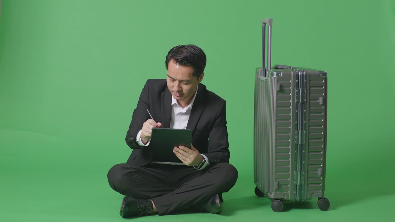 녹색 화면 배경 스튜디오에 앉아있는 동안 태블릿에 메모를 취하는 짐과 함께 아시아 사업가 여행자의 전체 몸