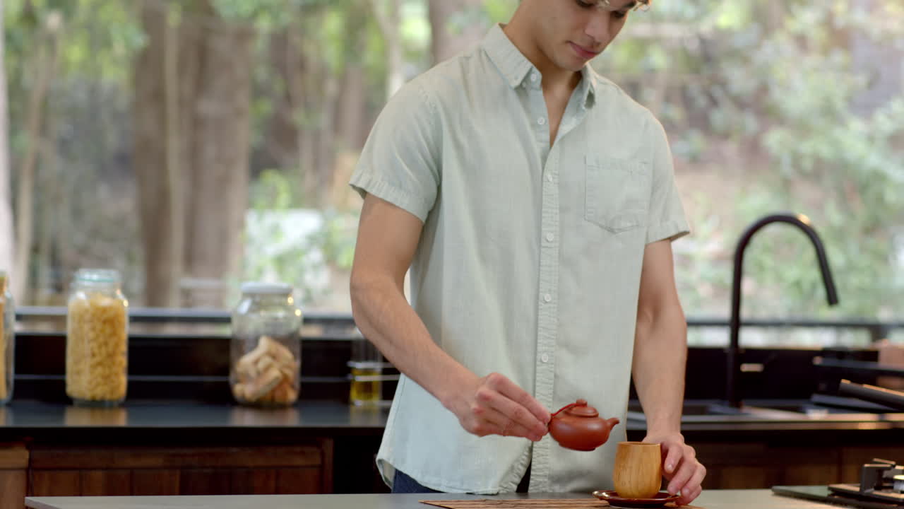 Young man in kitchen looking thoughtful, surrounded by jars and greenery