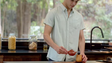 young man in kitchen looking thoughtful, surrounded by jars and greenery