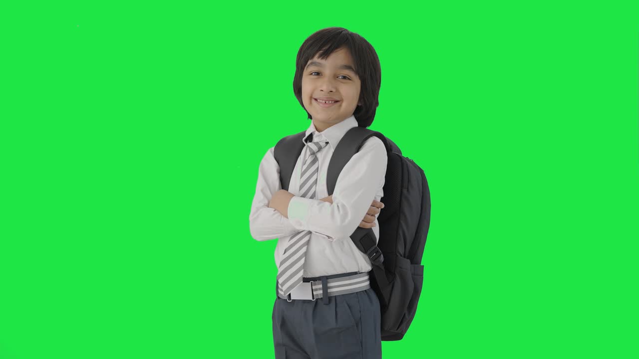 retrato de un niño de escuela indio feliz de pie con las manos cruzadas pantalla verde