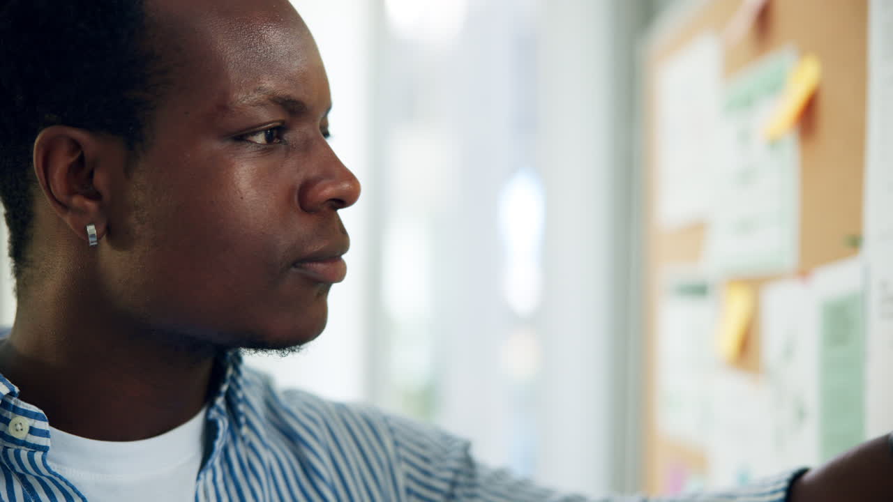 Focused Young African American Man Reviewing Notes on Cork Board