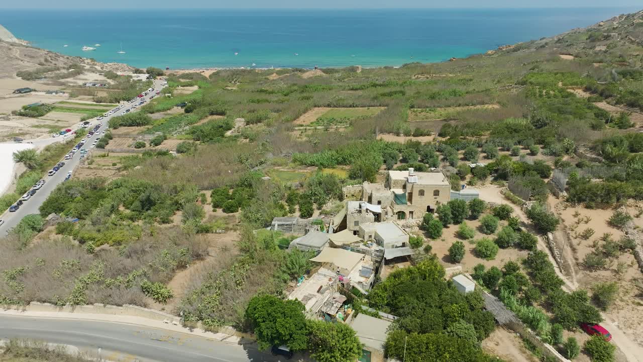 el dron captura una amplia vista aérea de una playa costera con aguas azules profundas del océano, destacando barcos, bañistas y formaciones costeras naturales y el campo en el fondo