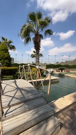 a view of a building with wooden bridge and fountain overlooking on lake, close up shot