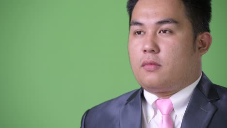 young handsome overweight asian businessman against green background