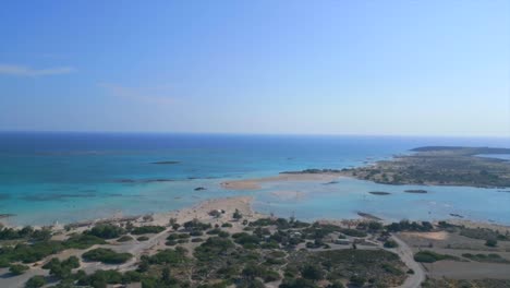 capture elafonisi beach in crete with drone footage. the shot begins with showing of the island's lush vegetation and gradually ascends to reveal the shallow waters connecting crete to elafonisi