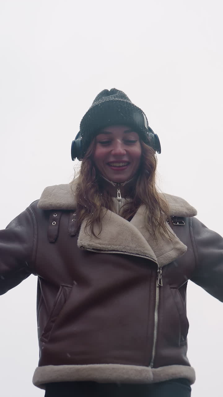 Close view of happy lady in black knit cap, brown shearling jacket with arms outstretched while walking joyfully on a cool autumn day in peaceful outdoor setting