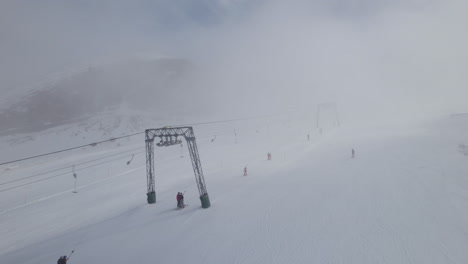 Aerial-flyover-Skier-skiing-snowy-slope-during-foggy-day-beside-ski-lift-in-Austria