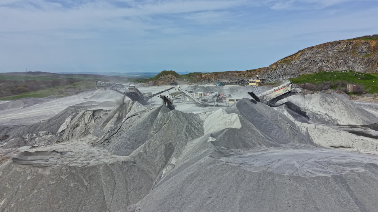 Operación de cantera de granito con maquinaria y pilas de piedra bajo un cielo despejado.