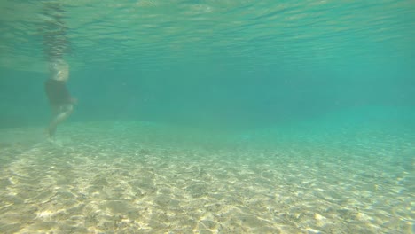 Junger-Mann,-Der-In-Einem-Natürlichen-Wasserfall-Spazieren-Geht,-Blaues,-Klares-Wasser,-Unterwasseraufnahme