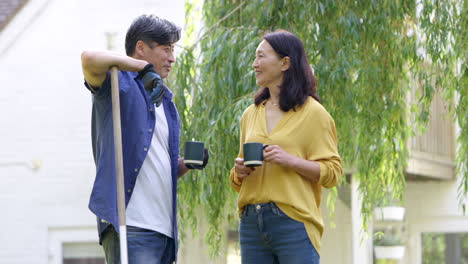 mature asian couple taking a break from tidying leaves in garden chatting whilst drinking hot drink - shot in slow motion