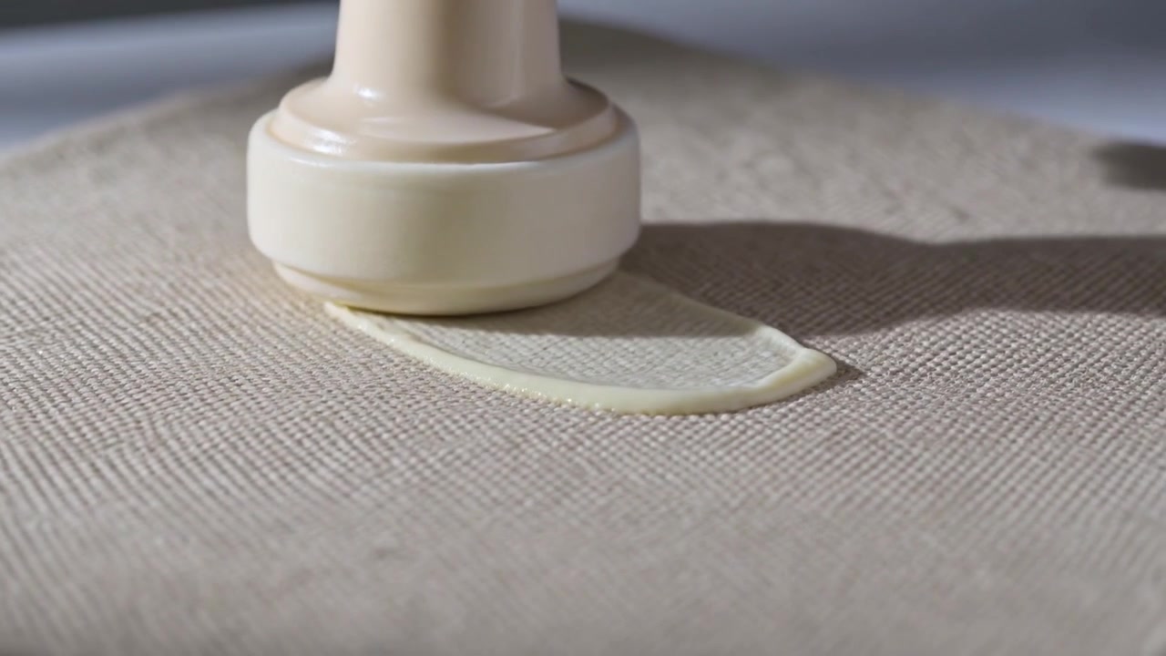 Pressing plastic nozzle onto beige fabric hand extruding cream ribbon dragging crescent to adhere