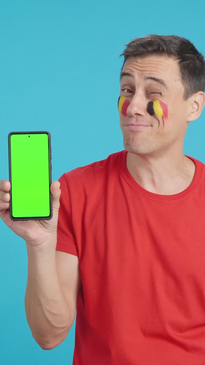 Belgian supporter looking at his mobile smiling and showing it