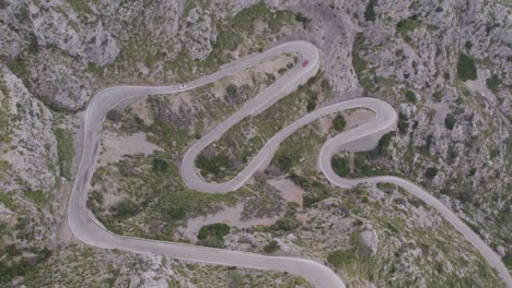 Top-down-shot-of-car-driving-at-mountain-pass-Coll-dels-Reis-Mallorca-during-day-time,-aerial