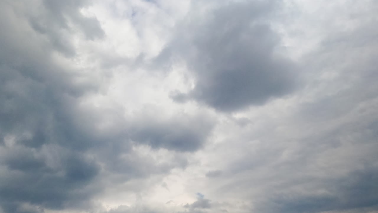 Azure sky hardly ever seen behind the grey cloudscape. Grey clouds accumulating in the atmosphere. Low angle view. Timelapse.