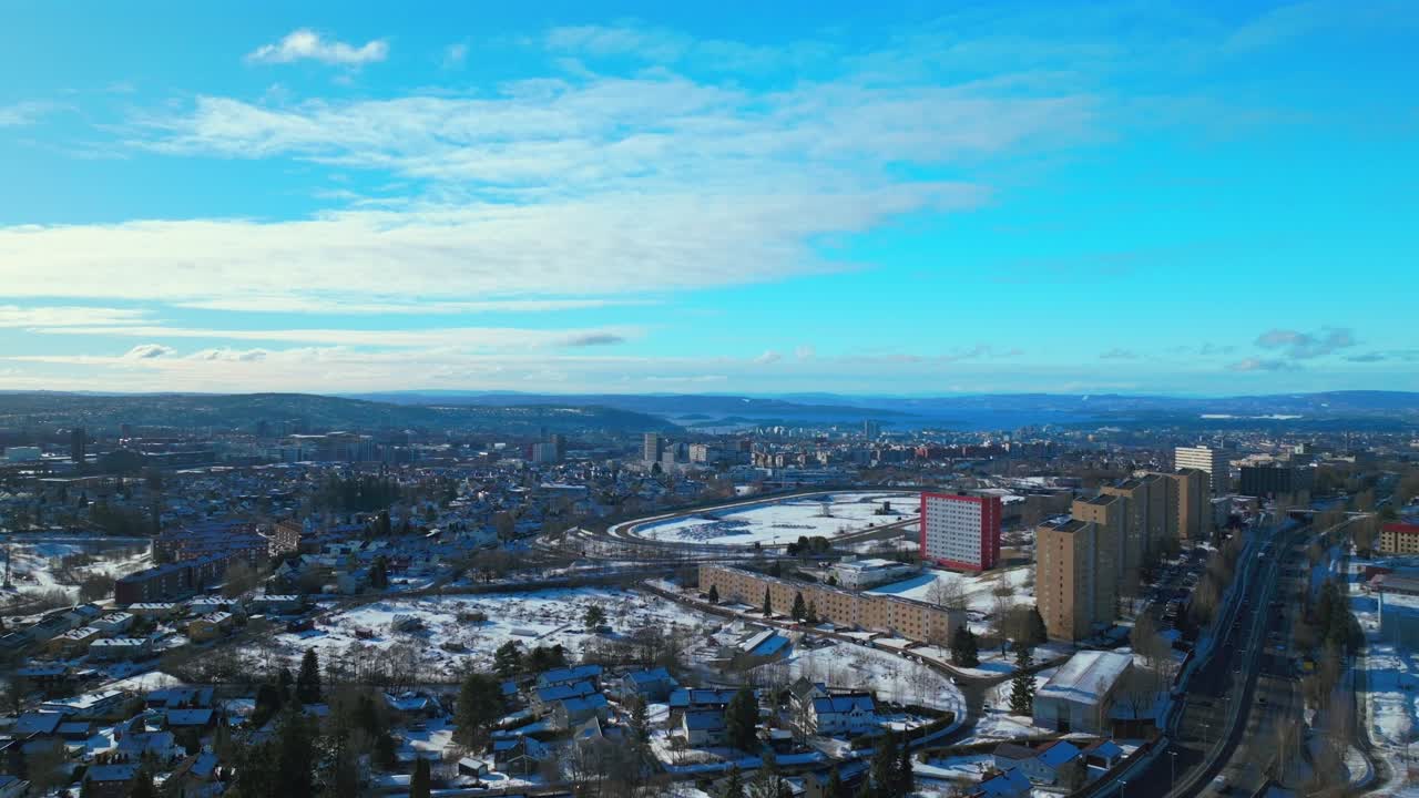 Sunny blue sky daytime Oslo race track Norway Norge aerial drone Norwegian winter Bjerke Travbane Tonsenhagen apartment buildings Nordmarka forest icy snowy car highway upwards