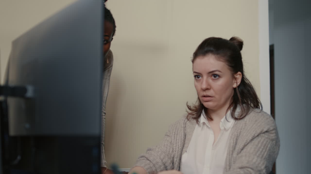 Junior developer writing source code under senior dev supervision sitting at desk with multiple screens