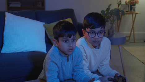 two young boys at home playing with computer games console on tv holding controllers late at night 1