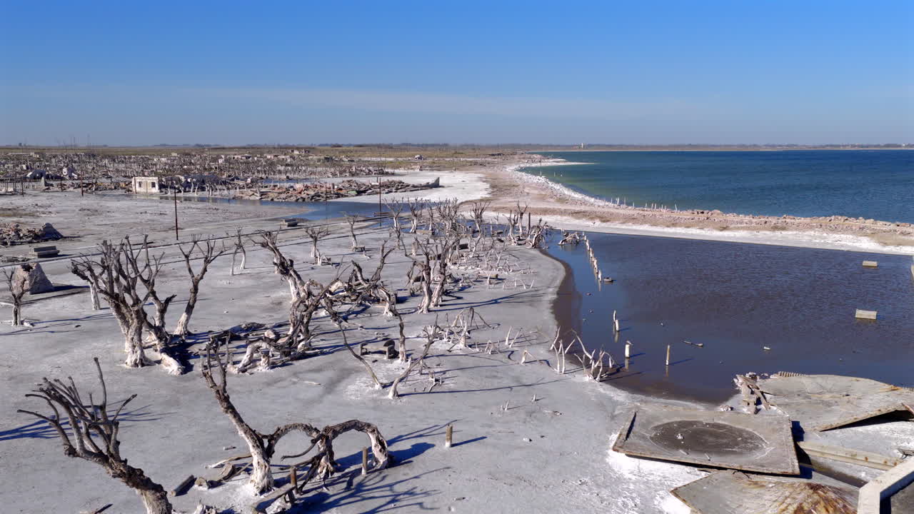 Low-altitude drone glides forward above submerged ruins of Epecuén village in the lake on a sunny day