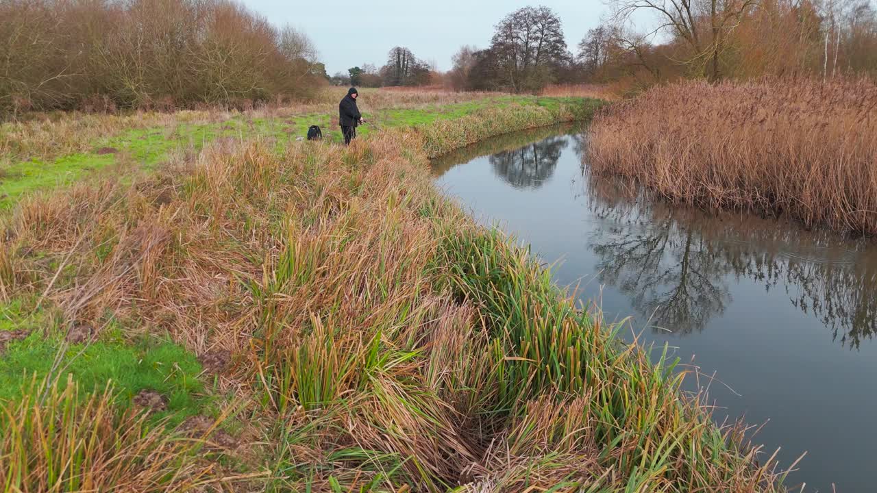 Hooded old man angling in a river in Northern Europe. Aerial