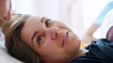 face of a woman who has just given birth to a baby. newly-made mom holds a newborn on chest and smiles to her husband. close up.